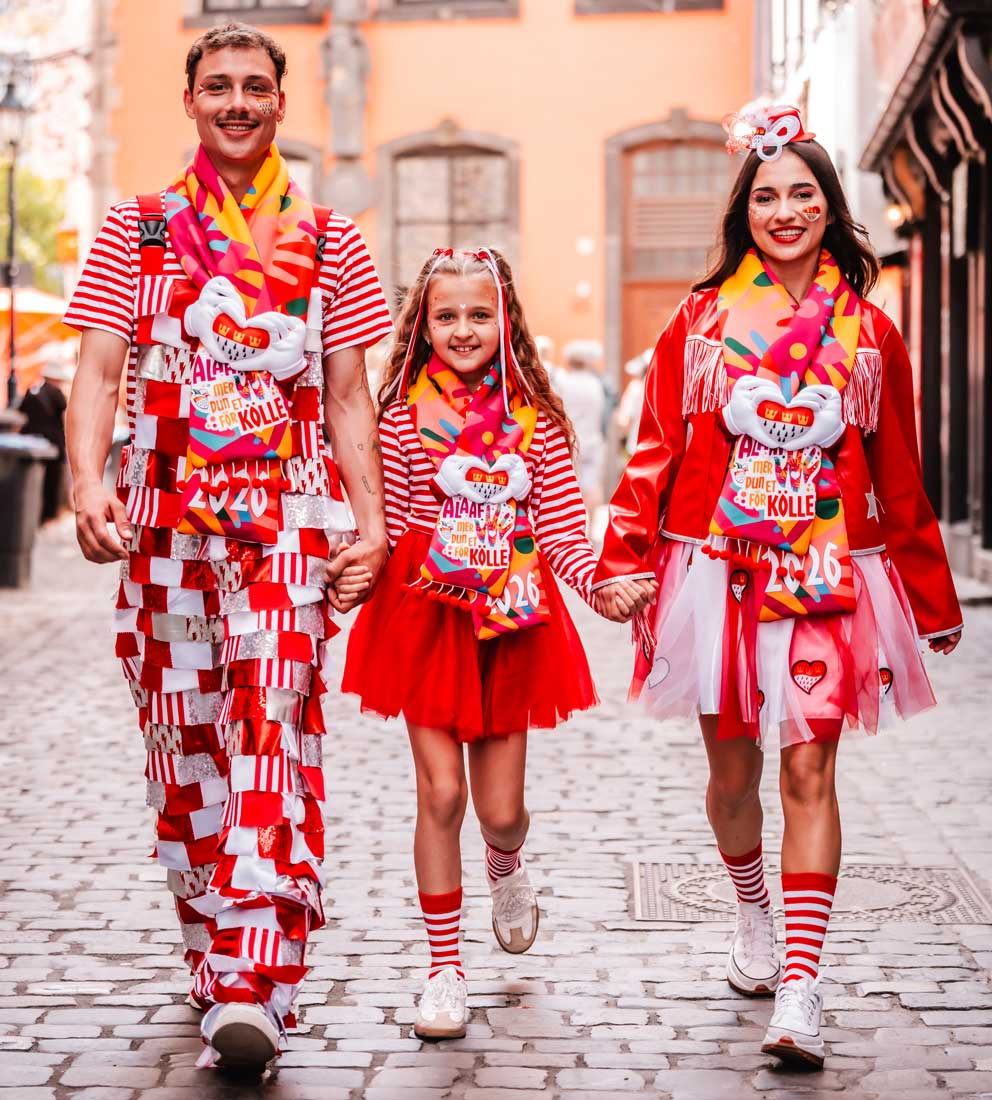 3 Personen mit dem Kölner Mottoschal 2025/2026 und in rot-weißen Kostümen